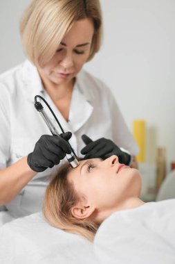 Rejuvenating facial therapy treatment at spa salon clinic. Young beautiful woman getting lifting anti-aging, face massage and skincare by electroporation facial therapy aesthetic cosmetology.