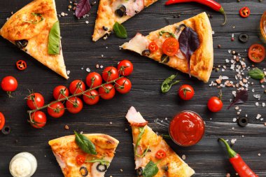 Kurutulmuş, zeytinli, peynirli ve otlu pizza dilimleri koyu ahşap arka planda, taze vişneli domates, sos ve pizza üst görünümü için baharatlarla servis edilir. İtalyan yemeği..