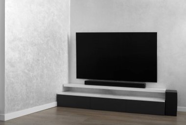 Oturma odasının içinde duvarında televizyon, hifi ekipmanları, ses çubuğu, gri dolap olan bir yer. Televizyon ve müzik sistemi iç kısımda. Parlak renklerle modern oturma odası.