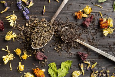 Antika kaşıklar, kuru amber çiçeği, lavanta çiçekleri ve koyu ahşap arka plan manzaralı koyu siyah ve yeşil çay karışımı. Koyu arkaplanda farklı türde kuru çay..