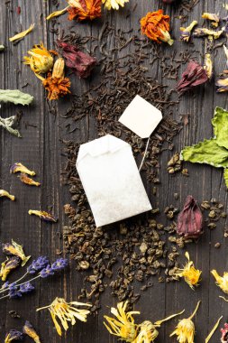 Kuru siyah ve yeşil çay, çay poşeti ve kuru amber çiçeği, takvim, lavanta çiçekleri ve yakın plan koyu ahşap arka plan görüntüsü. Koyu arkaplanda farklı türde kuru çay..