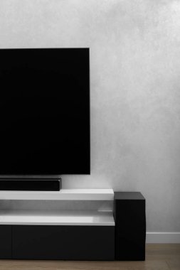 Part of modern living room interior with place for text. Decorative plaster for walls. Interior details. Flat TV on the wall in the living room. White shelf in the room. The wall is grey.