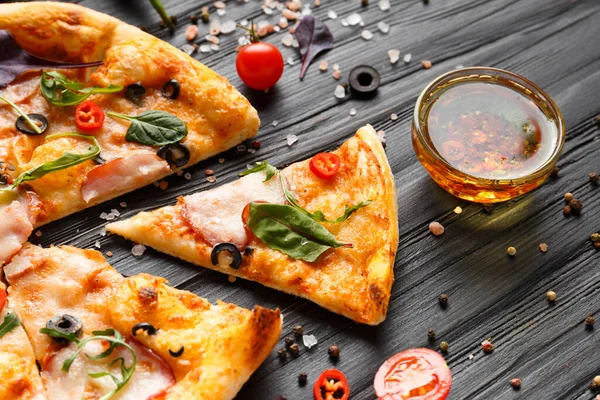 Pizza with jerky, cheese, sliced pizza slice, sauce, fresh vegetables and spices on a dark wooden background.