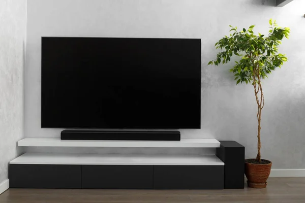 Stock image Part of the interior of the living room with a TV on the wall, hifi equipment, Sound bar, gray cabinet and a large indoor flower. TV and music system in the interior.