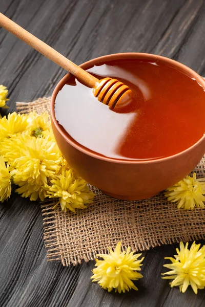蜂蜜在一个粘土碗 斗牛士和黄色的花在纺织品和黑暗的木制背景 一根蜂蜜棒放在装有蜂蜜特写的陶瓷碗里 — 图库照片