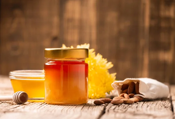 蜂蜜在一个封闭的玻璃瓶和一个碗 粘蜂蜜和分散的杏仁在木制背景 蜂蜜罐 坚果的成分在一个包的特写 健康食品 — 图库照片