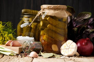 Koyu ahşap arka planda kapalı ve açık kavanozlarda salatalık turşusu. Salamura için ev yapımı salatalık, baharat ve otlar..