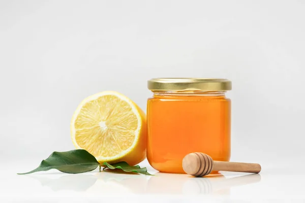 有机蜂蜜在一个封闭的透明玻璃瓶 木制斗篷和切碎柠檬绿色叶子隔离在一个白色的背景 蜂蜜和柑橘类水果特写 健康食品 — 图库照片