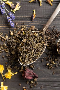 Antika kaşıklar, kuru amber çiçeği, lavanta çiçekleri ve koyu ahşap arka plan manzaralı koyu siyah ve yeşil çay karışımı. Koyu arkaplanda farklı türde kuru çay..