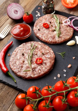 Çiğ kıymalı burger köfteleri, biberiye, sebze ve baharatlar ahşap bir arka planda siyah bir taş tabakta. Hamburger için malzemeler..