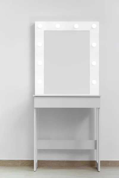 A white makeup dressing table with a large mirror and lights on against the wall. Makeup artist\'s workplace, modern dressing room.