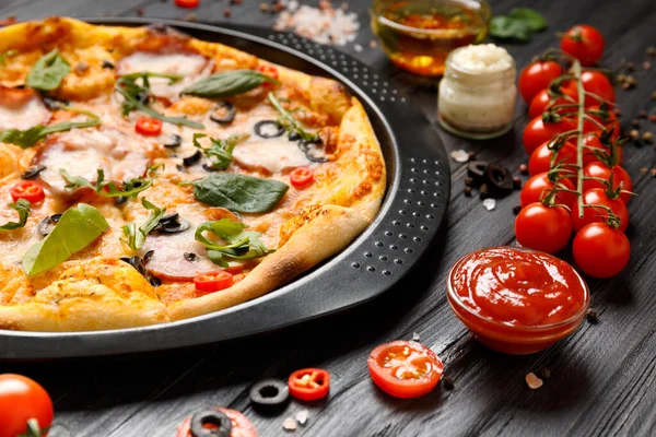 Kurutulmuş et, zeytin, peynir ve otlar, soslar, zeytin yağı ve siyah ahşap arka planda taze sebzeli pizza. Geleneksel İtalyan yemekleri.