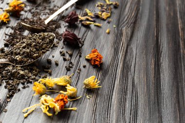 Antika kaşıklardaki kuru siyah ve yeşil çay kompozisyonu, koyu ahşap arka planda yakın plan görüntüsünde kuru çiçek çayı. Koyu arkaplanda farklı türde kuru çay..