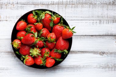 Hafif ahşap zemin üzerinde siyah yuvarlak bir tabakta taze organik çilekler, üst manzara, metin için yer var..