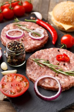 Çiğ kıymalı burger köfteleri, biberiye, sebze ve baharatlar ahşap bir arka planda siyah bir taş tabakta. Hamburger için malzemeler..