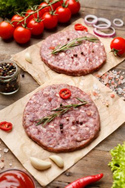 Baharatlı hamburgerler ve parşömen, sos, taze sebze, ahşap zeminde hamburgerler..
