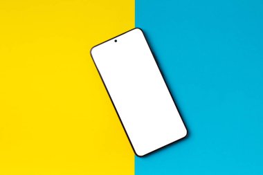 Parlak iki tonluk sarı-mavi arkaplanda beyaz ekranlı akıllı telefon, üst görünüm, boşluğu kopyala.