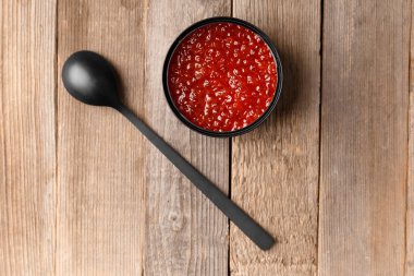 Açık siyah teneke kutuda kırmızı somon havyarı ve tahta arka planda siyah bir kaşık. Lezzetli deniz ürünleri, konserve balıklar..