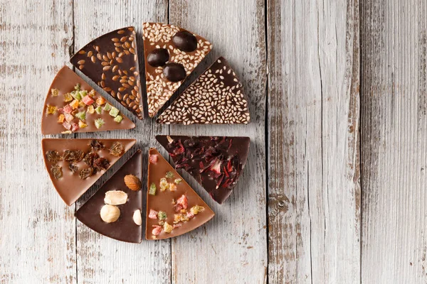 Creative composition chocolate in the shape of a pizza with candied fruits, nuts, dry berries, chocolate pizza and ingredients on a wooden background copy space.