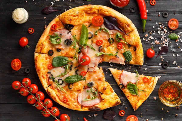 Etli pizza, dilimlenmiş, bir dilim ayrılır, taze kiraz domatesleri, soslar ve baharatlar koyu ahşap arka planda, üst manzara