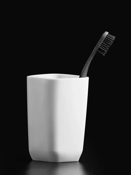 黒い背景に隔離された白い不透明なガラスの黒い歯ブラシ — ストック写真