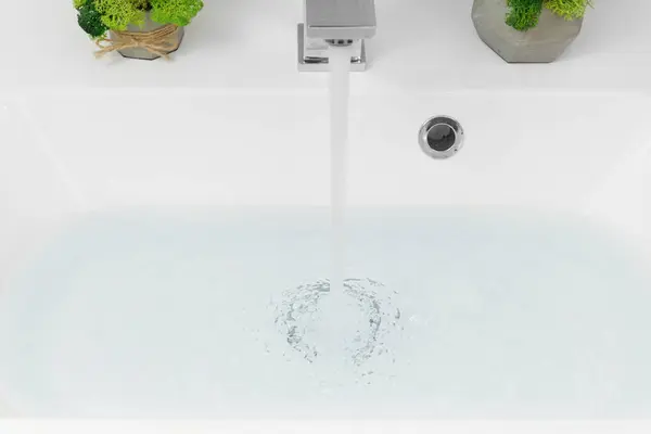 白い洗面台の近くにクロム蛇口から水が注ぐ 水資源を節約し 天然資源を保護するという概念 — ストック写真