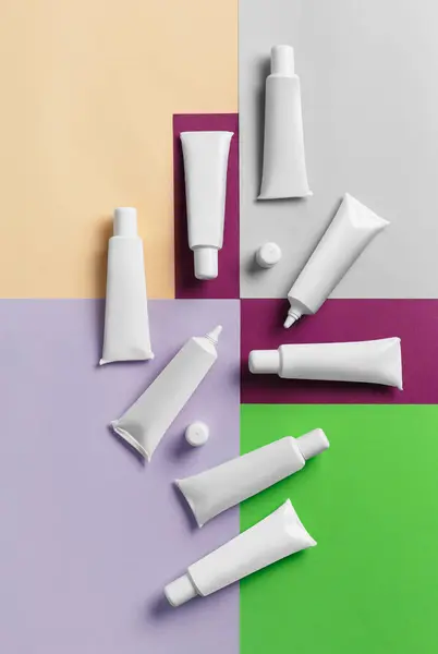 White tubes of packaging for cosmetics, paint, glaze on a multi-colored bright background, top view. Concept of cosmetics, medicine. Products for artists, confectioners.