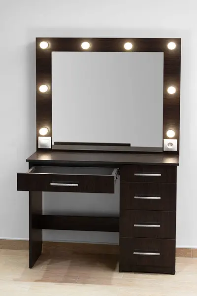 Dark makeup dressing table with a large mirror and lamps against a white wall. Makeup artist\'s workplace, modern dressing room.