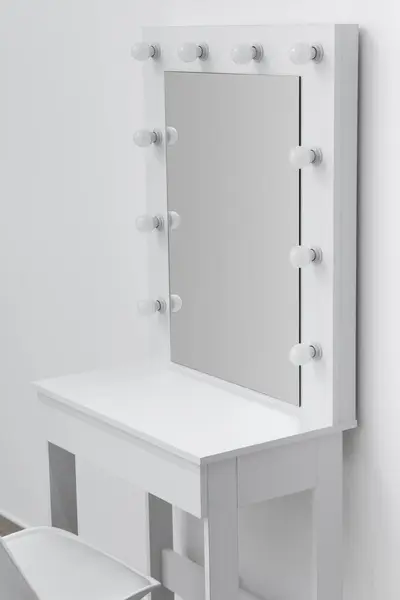 White makeup dressing table with a large mirror and lights on against the background of the wall close-up. Makeup artist\'s workplace, modern dressing room.