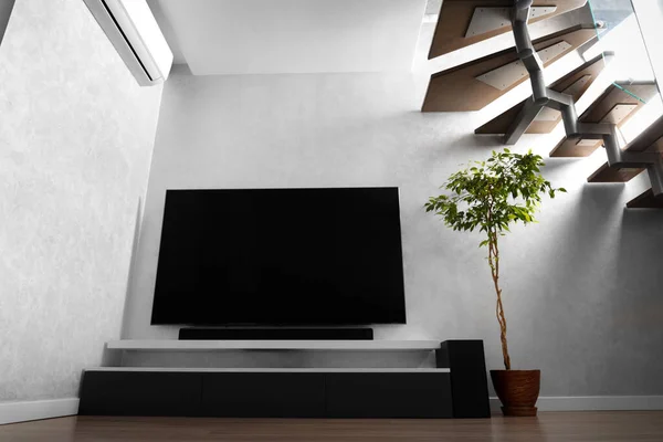 Part of the interior of the living room with a TV on the wall, hifi equipment, Sound bar, gray cabinet and a large indoor flower. TV and music system in the interior.