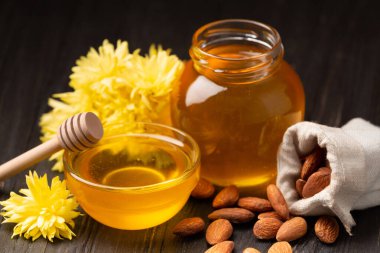 Cam kavanozda bal ve bir kase, bal için çubuklar ve ahşap arka planda dağınık bademler. Bal kavanozu, çerez ve fındık karışımı..