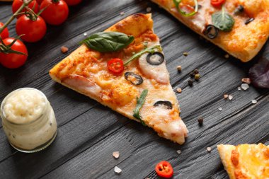 Kurutulmuş, zeytinli, peynirli ve otlu pizza dilimleri koyu ahşap arka planda, taze vişneli domates, sos ve pizza üst görünümü için baharatlarla servis edilir. İtalyan yemeği..