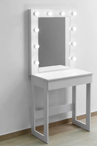 A white makeup dressing table with a large mirror and lights on against the wall. Makeup artist\'s workplace, modern dressing room.