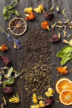 Kuru siyah ve yeşil çay, kurutulmuş narenciye dilimleri, nane yaprakları ve koyu ahşap arka plan manzaralı kuru amber çiçekleri. Koyu arkaplanda farklı türde kuru çay..