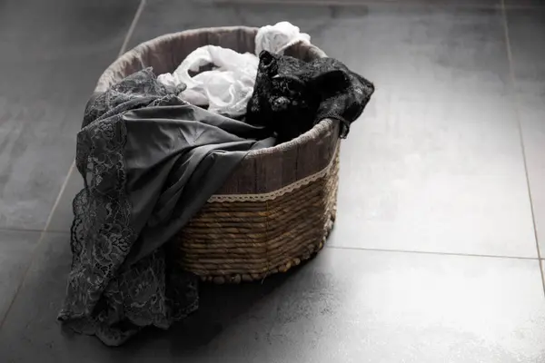 stock image Conceptual composition, women's underwear in a wicker basket for dirty laundry on a black background. A filled laundry basket against a dark floor.