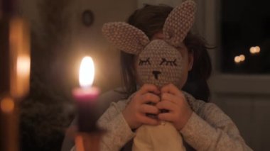 Ön dişleri olmayan bir kız oyuncak tavşanı indirir ve gülümseyen kameraya bakar.