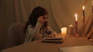 Kız oyuncak arkadaşına elinde bir tavşan tutuyor, ve gözlüklü bir kitap okuyor, mum ışığında burnunun köprüsünü göz yorgunluğundan siliyor.