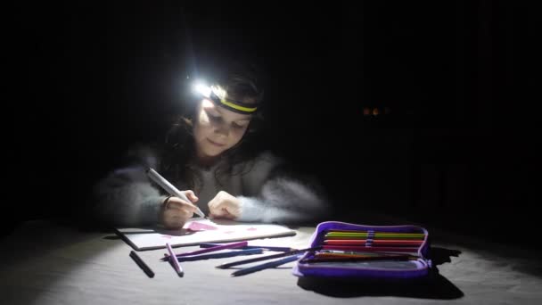 女の子の頭の上の懐中電灯からの唯一の光源を持つ電気のない暗いアパートで 子供は フェルト先端ペンで心を描きます — ストック動画