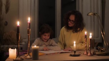 mother helps to do homework praises and hugs her daughter by candlelight