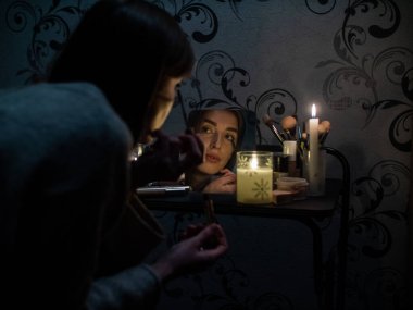woman doing makeup in a dark apartment by candlelight