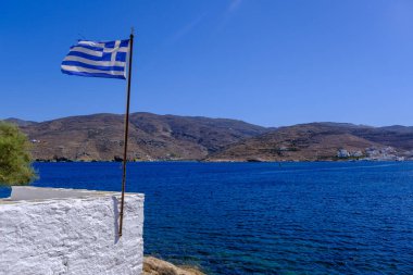Tinos Adası 'nda mavi gökyüzü ve denizin üzerinde dalgalanan Yunan bayrağı