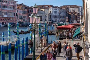 Venedik, İtalya - 12 Ekim 2024: Büyük Kanal boyunca uzanan tarihi binalarla Rialto Köprüsü yakınlarındaki bir rıhtım boyunca yürüyen turistler.