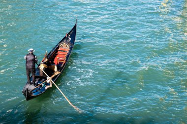 Venedik, İtalya - 12 Ekim 2024: Klasik çizgili bir gondolcu geleneksel Venedik gondoluyla parıldayan suları aşıyor.