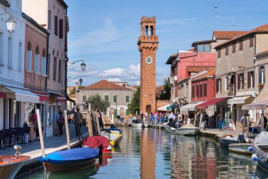 Venedik, İtalya - 12 Ekim 2024: Torre dellOrologio, tarihi bir kırmızı tuğlalı saat kulesi Murano 'nun sakin kanalları üzerinde yükselir ve zengin Venedik mirasını yansıtır.