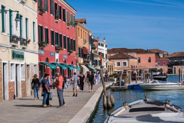 Venedik, İtalya - 12 Ekim 2024: Murano 'nun renkli binalar, dükkanlar ve kanala bakan restoranlarla dolu canlı rıhtım gezisi turistler