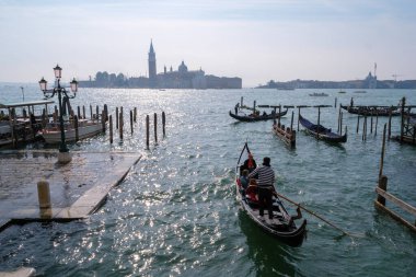 Venedik, İtalya - 12 Ekim 2024: Geleneksel gondollar San Giorgio Maggiore yakınlarındaki Venedik Gölünün parıldayan sularında geziniyorlar