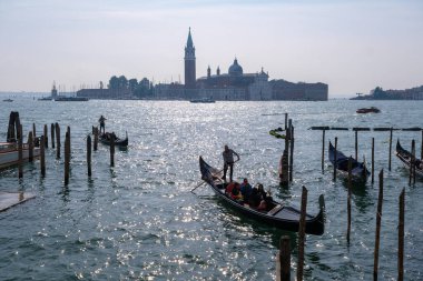 Venedik, İtalya - 12 Ekim 2024: Geleneksel gondollar San Giorgio Maggiore yakınlarındaki Venedik Gölünün parıldayan sularında geziniyorlar