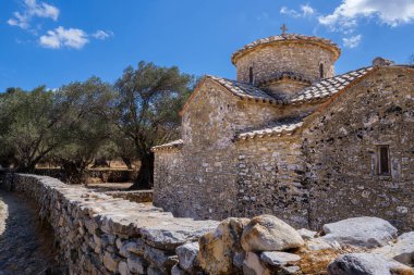 Naxos 'taki Aziz George Diasoriti Kilisesi, açık mavi gökyüzünün altında zeytin ağaçları ve tepelerle çevrili kırmızı kiremitli küçük bir taş kilise.