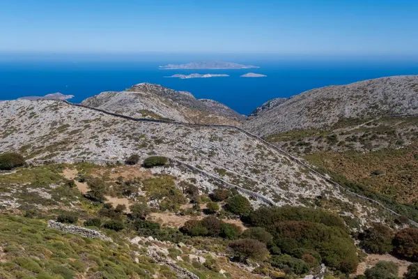 Zeus Dağı 'nın manzaralı manzarasında yemyeşil ve geleneksel taş duvarları olan dağlık arazi, açık gökyüzünün altındaki adaların yakınlarındaki derin mavi Ege Denizi' ne bakıyor.