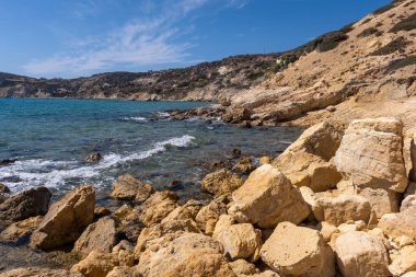 Agios Sostis sahilinin kayalık kıyılarında turkuaz sular altın kayalarla buluşur.